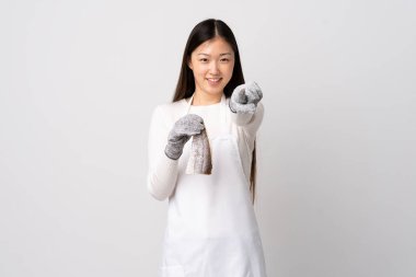 Çinli balıkçı önlük takıyor ve elinde çiğ bir balığı izole edilmiş beyaz arka planda tutuyor mutlu bir ifadeyle ön tarafı işaret ediyor.