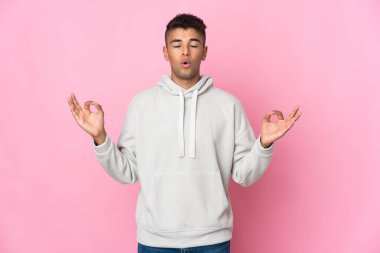 Zen pozisyonunda pembe arka planda izole edilmiş genç Brezilyalı adam.
