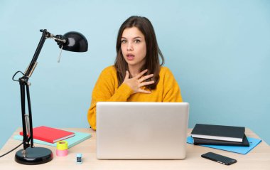 Öğrenci kız evinde çalışıyor. Mavi arka planda tek başına. Şok olmuş ve şaşırmış.