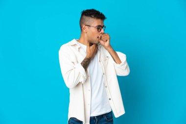 Genç Brezilyalı bir adam mavi arka planda çok öksürüyor.