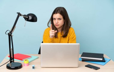 Evinde okuyan öğrenci kız mavi arka planda izole edilmiş hayal kırıklığına uğramış ve ön tarafı işaret ediyor.