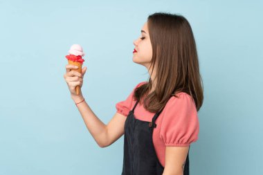Kornet dondurması tutan genç kız mavi arka planda mutlu bir ifadeyle izole edilmiş.