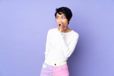 Mor arka planda kısa saçlı genç Vietnamlı kadın yan tarafa bakarken sürpriz bir jest yapıyor.