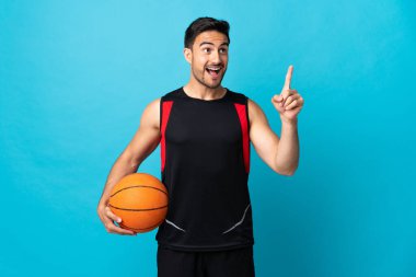 Genç yakışıklı adam mavi arka planda izole edilmiş basketbol oynuyor ve bir fikri var.