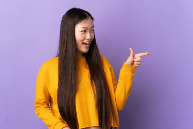 Mor arka planda izole edilmiş genç Çinli bir kız parmak göstererek bir ürün sunuyor.