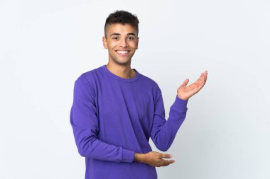 Beyaz arka planda izole edilmiş genç Brezilyalı adam, davet etmek için ellerini yana uzatıyor.