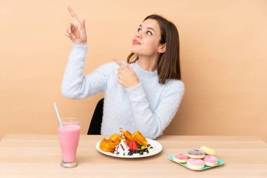 Bej arka planda izole edilmiş waffle yiyen genç kız işaret parmağıyla işaret etmek harika bir fikir.