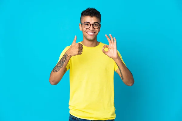 Młody Brazylijczyk Odizolowany Niebieskim Tle Pokazuje Znak Kciuk Górę Gest — Zdjęcie stockowe