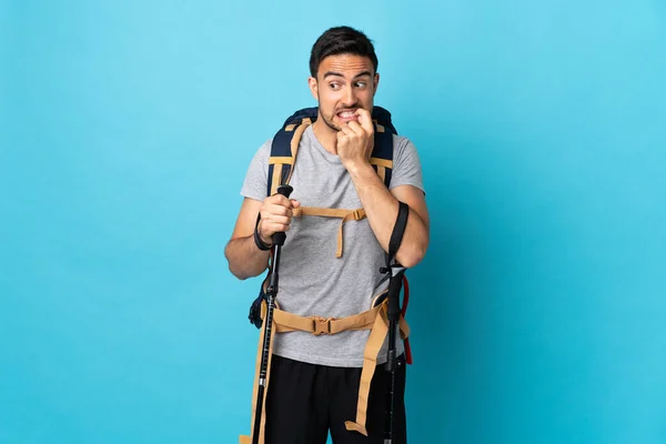 Jovem Caucasiano Com Mochila Postes Trekking Isolado Fundo Azul Nervoso — Fotografia de Stock