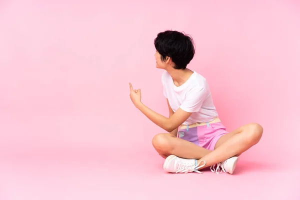 Jovem Vietnamita Com Cabelo Curto Sentado Chão Sobre Fundo Rosa — Fotografia de Stock