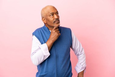 Kübalı son sınıf öğrencisi pembe arka planda izole edilmiş. Şüpheleri ve düşünceleri var.
