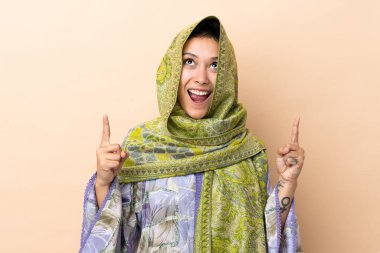 Indian woman isolated on beige background surprised and pointing up