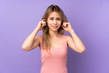 Teenager Russian girl isolated on purple background frustrated and covering ears