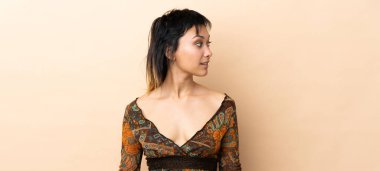 Bej arka planda izole edilmiş Hintli kadın yan tarafa bakıyor.