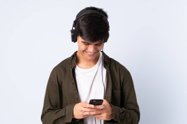 Handsome man over isolated blue background listening music and looking to mobile
