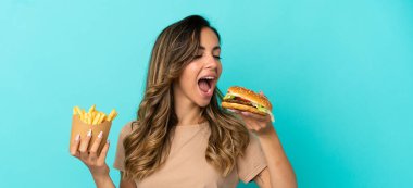 Arkaplanda kızarmış cips ve hamburger tutan genç bir kadın.