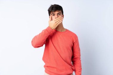 İzole edilmiş mavi arka planda yakışıklı bir adam. Ağzını eliyle kapatıyor.