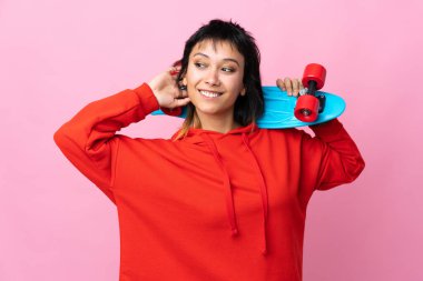 Genç Uruguaylı kadın izole pembe arka planda kaykayla geziyor.