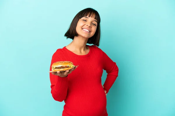 Młoda Kobieta Ciąży Trzyma Hamburgera Nad Odizolowanym Tle Pozowanie Ramionami — Zdjęcie stockowe