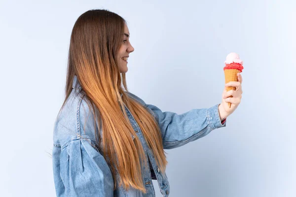 Young woman with a cornet ice cream isolated on blue background with happy expression