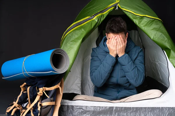 Teenager caucasian man inside a camping green tent isolated on black background with tired and sick expression