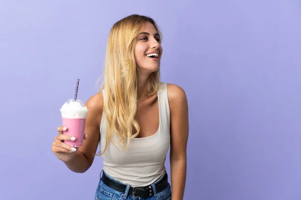 年轻的金发碧眼的乌拉圭女人 与草莓奶昔隔离在紫色的背景笑中 — 图库照片
