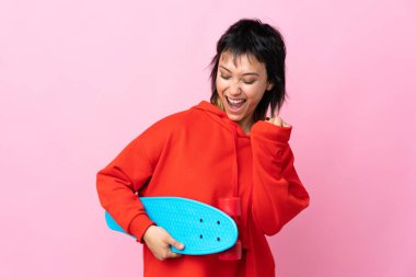 Genç Uruguaylı kadın izole pembe arka planda kaykayla geziyor.