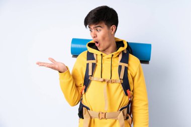 İzole edilmiş mavi arkaplan üzerinde büyük bir sırt çantası olan genç dağcı.