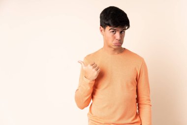 Handsome man over isolated beige background unhappy and pointing to the side