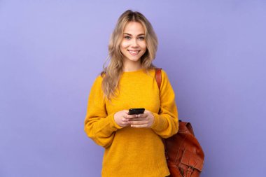 Teenager Russian student girl isolated on purple background sending a message with the mobile