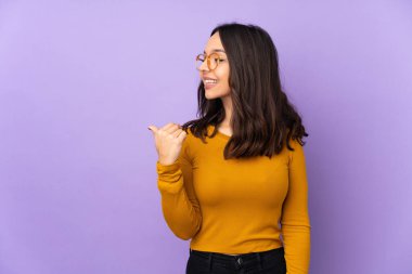 Mor arka planda izole edilmiş genç bir ırk kadını bir ürünü sunmak için kenarı işaret ediyor.