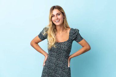 Genç sarışın Uruguaylı, mavi arka planda tek başına gülüyor.