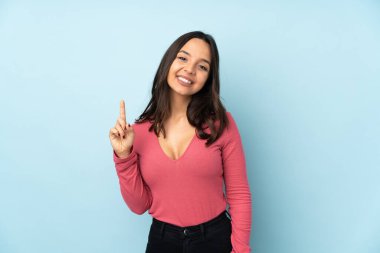 Mavi arka planda izole edilmiş genç bir ırk kadını en iyinin işareti olarak parmağını kaldırıyor.