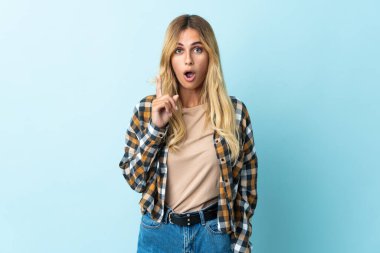 Genç sarışın Uruguaylı, mavi arka planda izole edilmiş bir şekilde parmağını kaldırarak çözümü anlamaya çalışıyor.