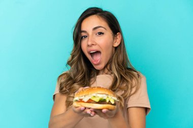 Arkaplanda hamburger tutan genç bir kadın.