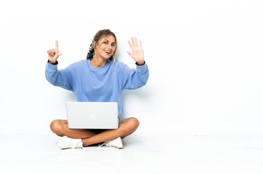 Dizüstü bilgisayarı olan genç sarışın Uruguaylı kız beyaz arka planda izole edilmiş, parmaklarıyla yediyi sayıyor.
