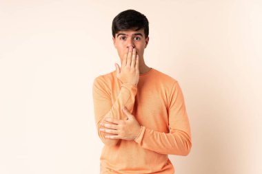 Handsome man over isolated beige background covering mouth with hand