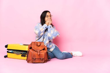 Elinde bavul olan gezgin kadın yere oturmuş ağzını kapatıyor ve yan tarafa bakıyor.