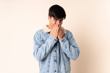 Handsome man over isolated beige background happy and smiling covering mouth with hands