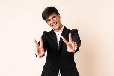 Businessman over isolated beige background smiling and showing victory sign