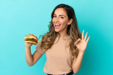 Arka planda hamburger tutan genç bir kadın parmaklarıyla tamam işareti gösteriyor.