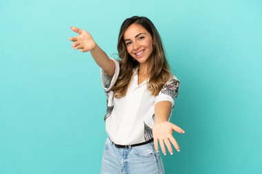 İzole edilmiş mavi arka planda genç bir kadın sunar ve davet eder.