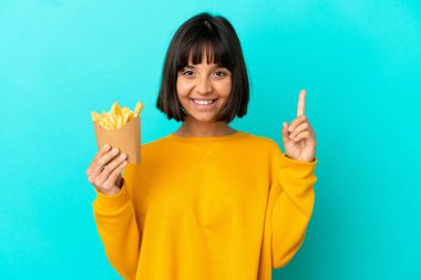 Genç esmer kadın izole edilmiş mavi arka planda patates kızartması tutarken harika bir fikre işaret ediyor.