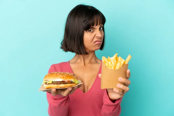 Jovem Morena Segurando Hambúrguer Batatas Fritas Sobre Fundo Azul Isolado — Fotografia de Stock