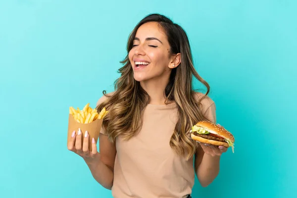 Young woman holding fried chips  and burger over isolated background