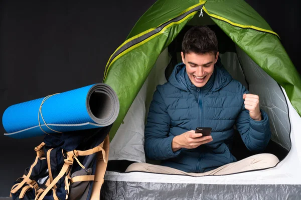 Teenager caucasian man inside a camping green tent isolated on black background surprised and sending a message