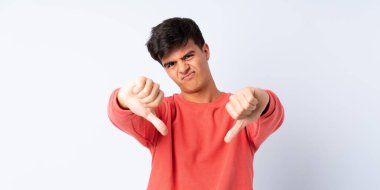 Soyutlanmış mavi arka planda yakışıklı bir adam baş parmağını iki eliyle aşağı gösteriyor.