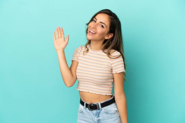 Soyutlanmış mavi arka planda genç bir kadın. Mutlu bir ifadeyle selamlıyor.
