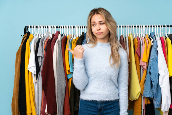 Teenager Russian girl buying some clothes isolated on blue background unhappy and pointing to the side