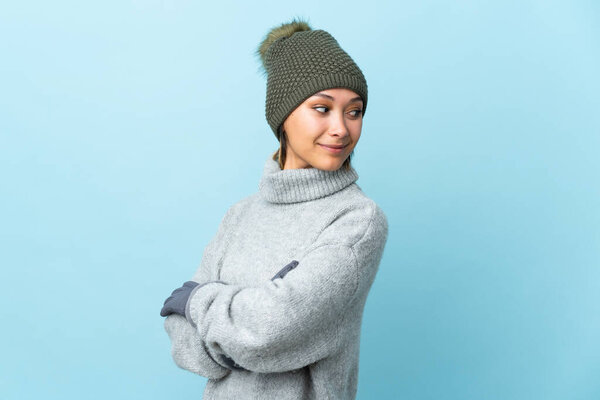 Young Uruguayan girl with winter hat isolated on blue background laughing